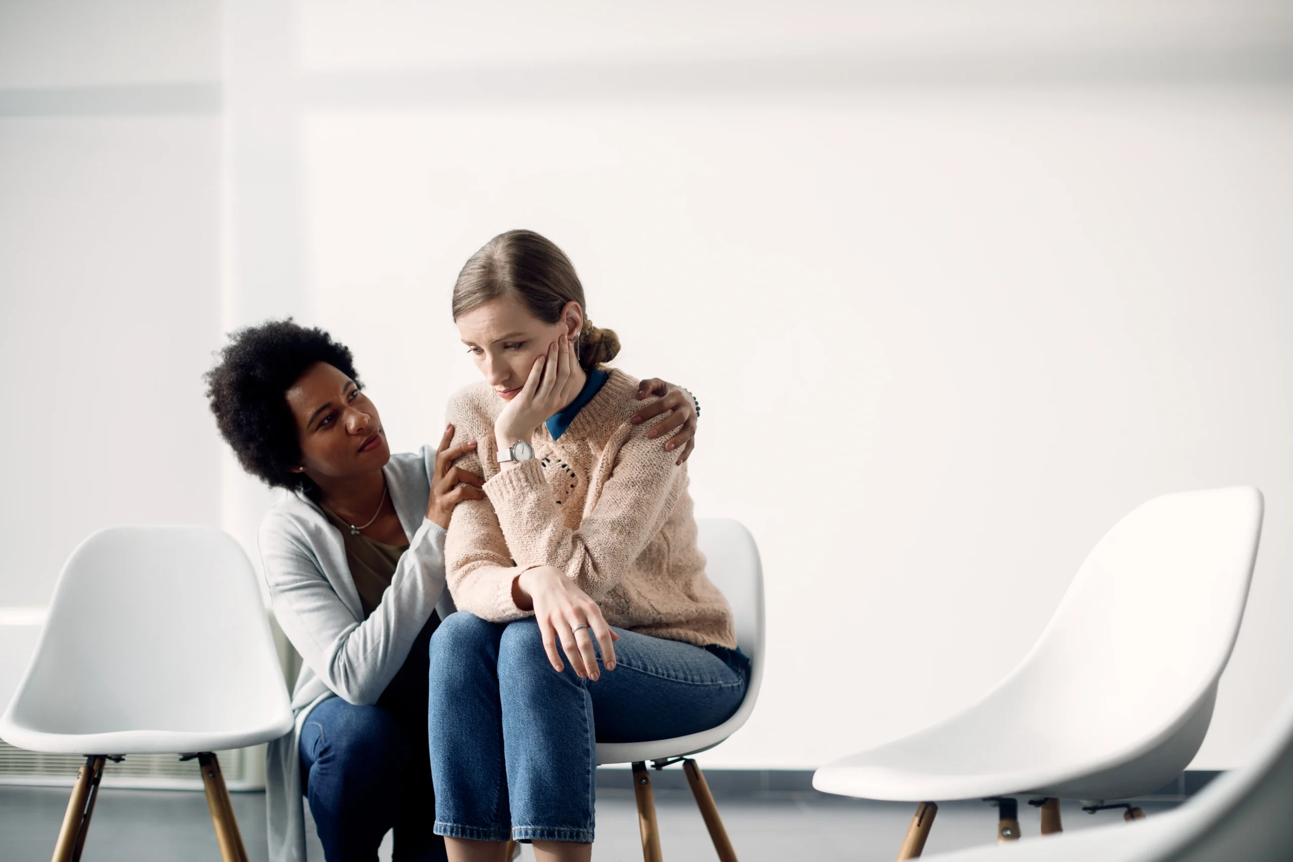 caring african american woman consoling sad woman before group therapy meeting
